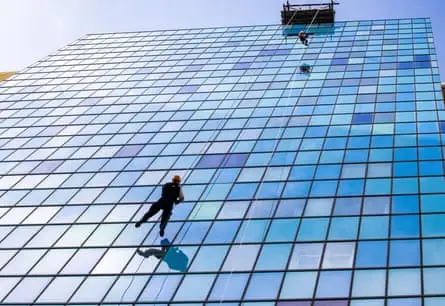 Figure abseiling down blue glass building.
