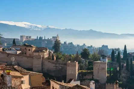 Skyline of Granada, Spain in winter with snowy mountains beyond and old walls in foreground