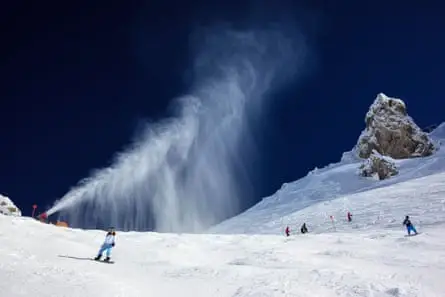 A snowcape against a deep blue sky with snow projecting from a small cannon-like machine