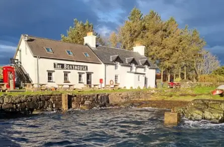 A harbour in front of a low cream building with the name The Boathouse in big letters on its facade