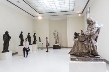 Sculptures in a well lit museum with people looking at them