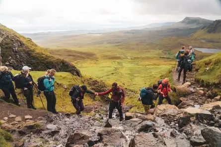 The walkers and a guide cross a stream on the Quiraing with views to Trotternish Ridge.