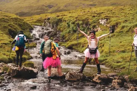Women crossing a river wearing tutus one with her arms outstretched calling out or singing