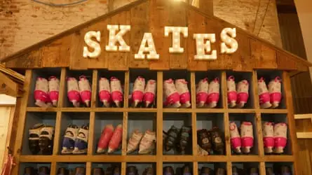 یک کابینت چوبی پر از کفش‌های اسکیت با تابلویی روشن با نوشته «Skates» در بالا
