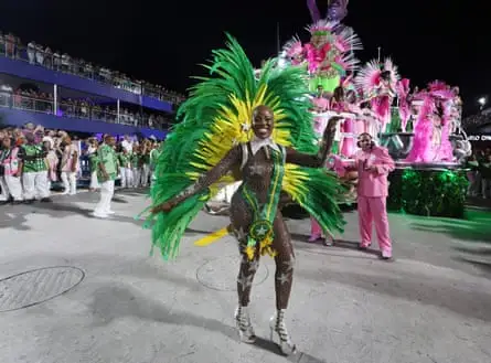 A  woman in a sheer bodysuit wearing yellow and green feathers and sash at a carnival parade in Rio de Janeiro, Brazil