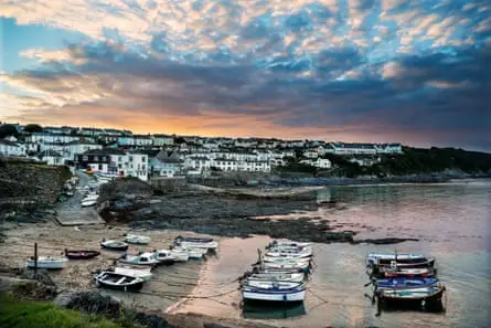 قایق‌هایی در یک بندرگاه کوچک در زمان جزر، با یک روستا در پس‌زمینه و غروب‌خیز گرفته