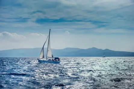 Yacht sailing in Adriatic sea with hilly rocky coast in the distance