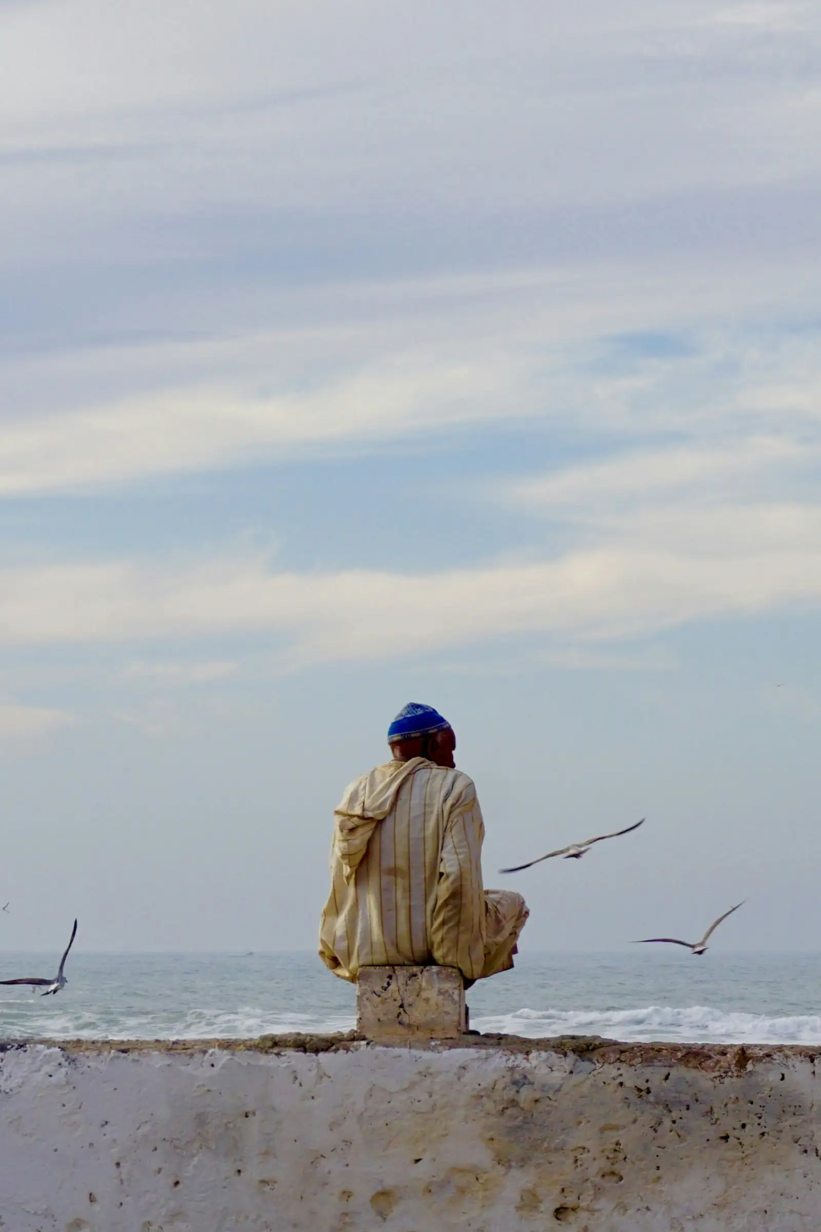مردی بربر بر روی دیواری رو به دریا نشسته است (پشتش به دوربین است)؛ اقیانوس در دوردست دیده می‌شود و مرغ‌های دریایی در اطراف پرواز می‌کنند.