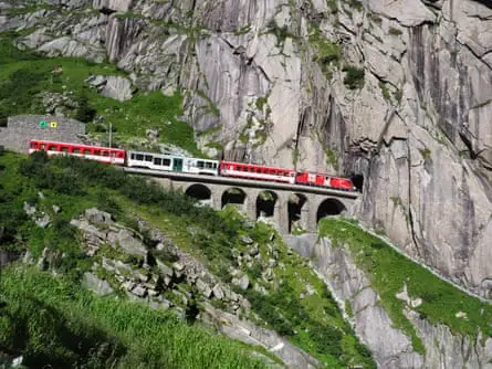 Red train on scenic stony St  Gotthard railway bridge and tunnel, swiss Alps 