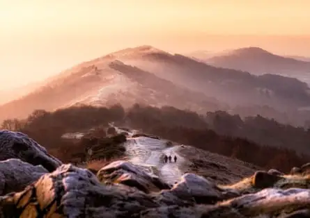 People walking a high ridge path in winter on a frosty day with lots of sun glow