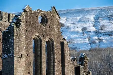 نمای جلوی ویرانه‌های صومعه قدیمی با دامنه تپه برفی در پس‌زمینه