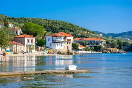 Sea, blue sky, green hills, and white buildings by shoreline